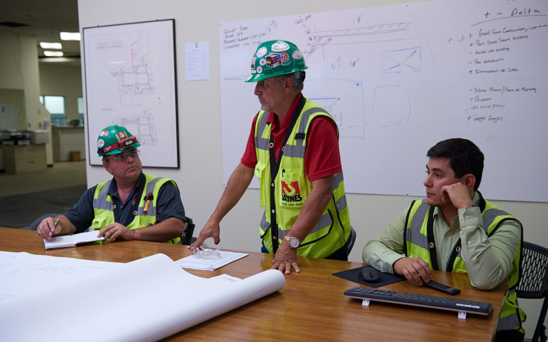 A crew of Jaynes employees and subcontractors gathers to listen to a Jaynes leader at a meeting in an unfinished construction site.