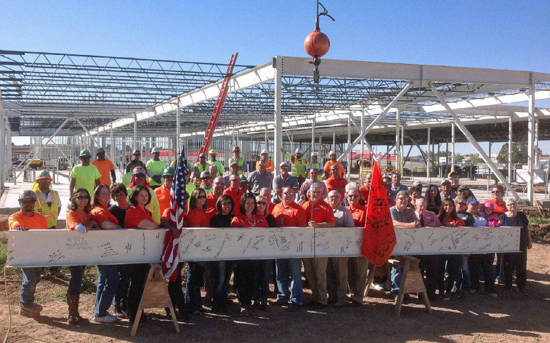 A large group of Jaynes crew members smiling and standing in front of a large metal beam.