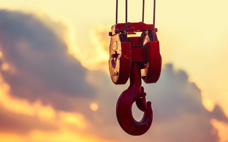 Large, red crane hook focused center frame with an orange, pink, and purple sunset in the background.
